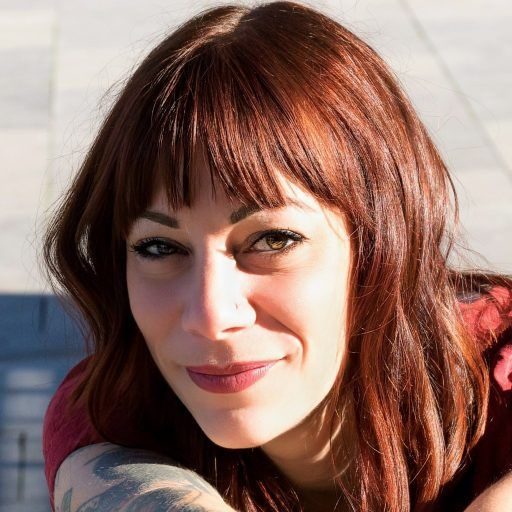 Céline Alice Garcia Hypnothérapeute à Niort Céline Alice Garcia souriante avec des cheveux roux et des tatouages, regardant vers l'objectif place de la Breche à Niort 79.